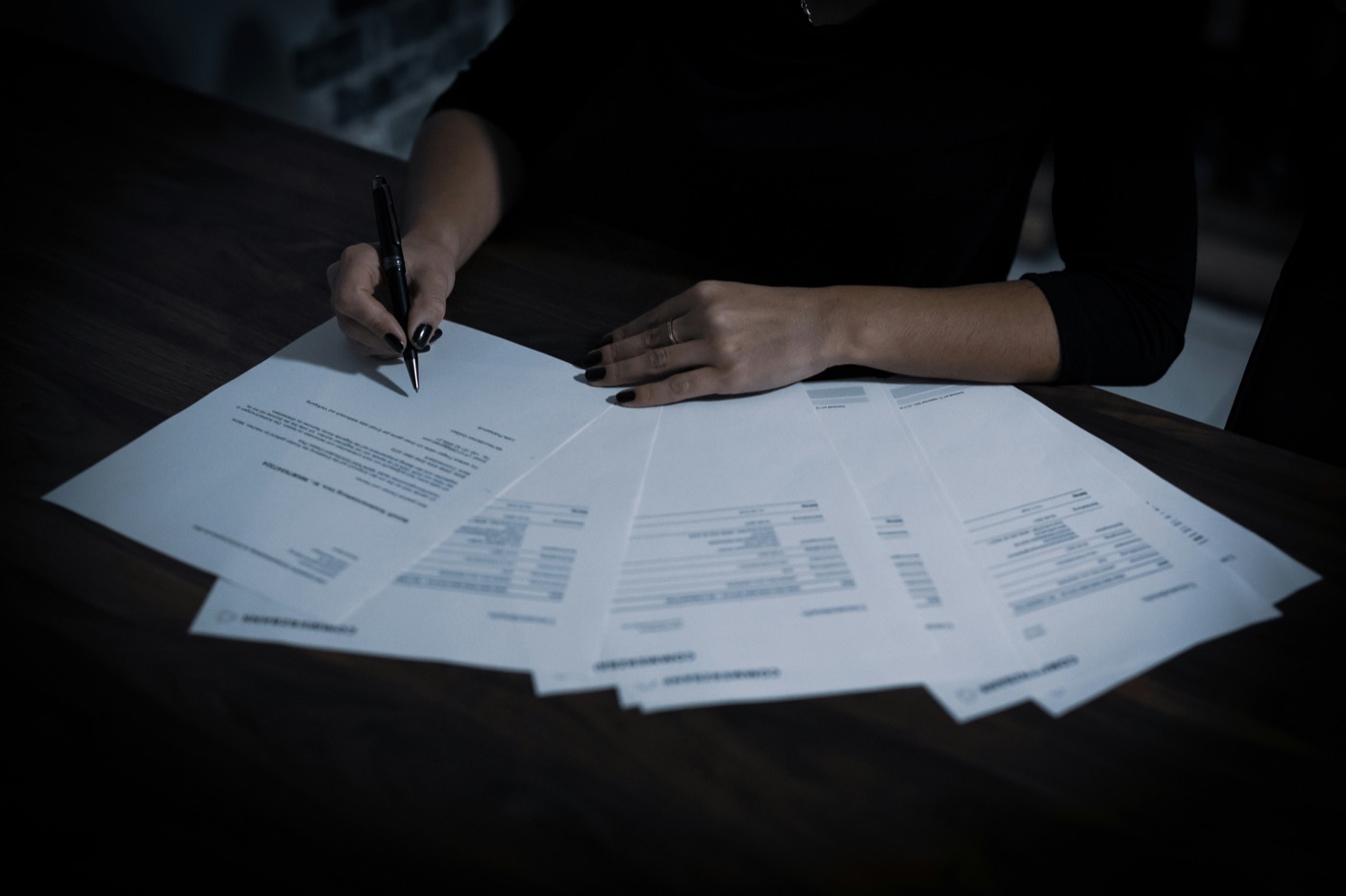 A hand signing a fanned-out stack of printed case files and forms, the kind of review Synthis accelerates.